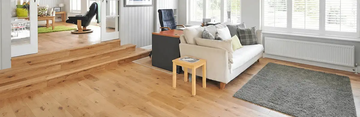 A modern living room with professionally installed laminate flooring, a beige sofa, a small side table, a gray rug, and large windows with white shutters in Orange, CA